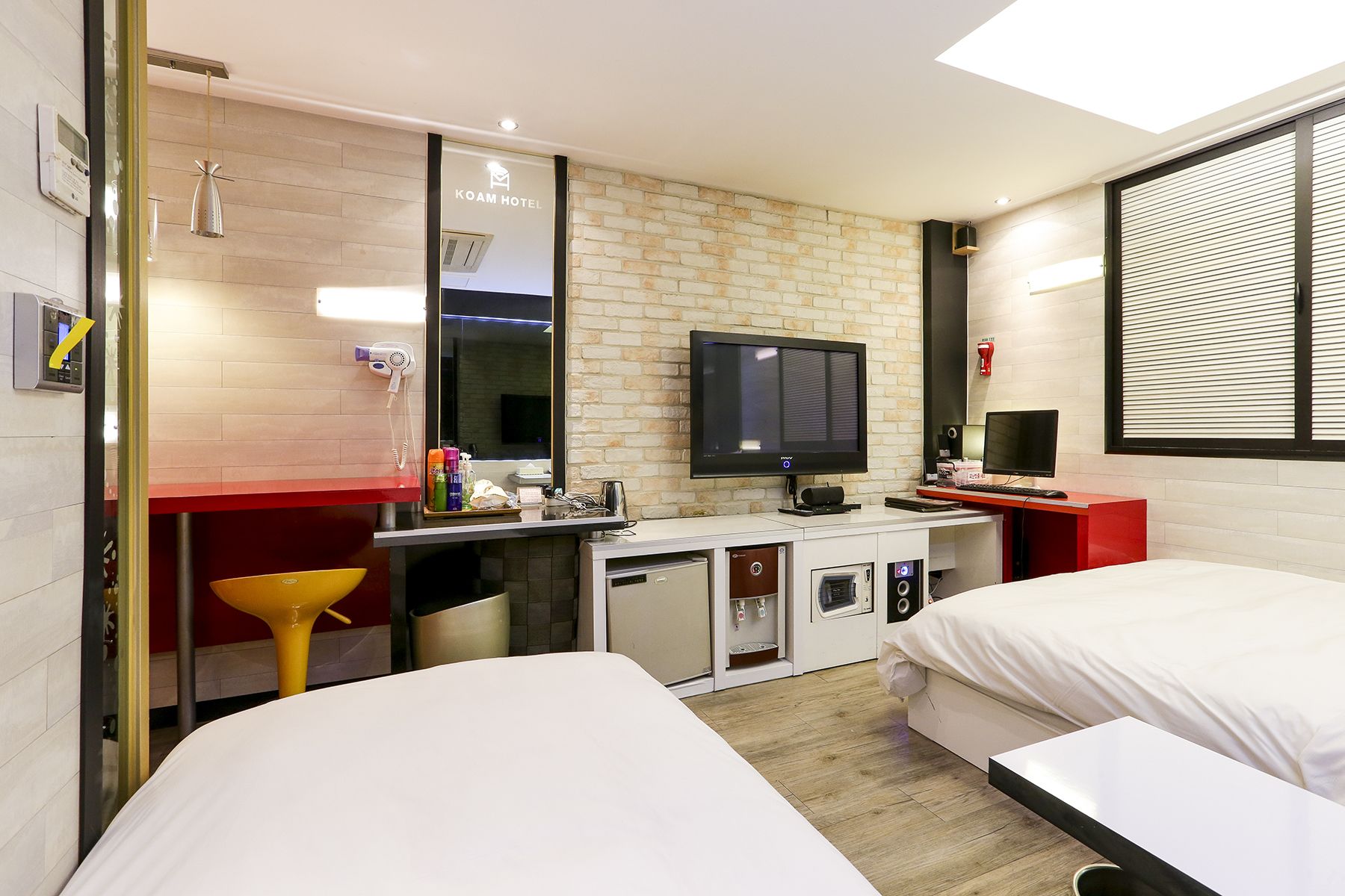 A hotel room with a bed, a desk with a computer, a TV, and a small kitchenette.