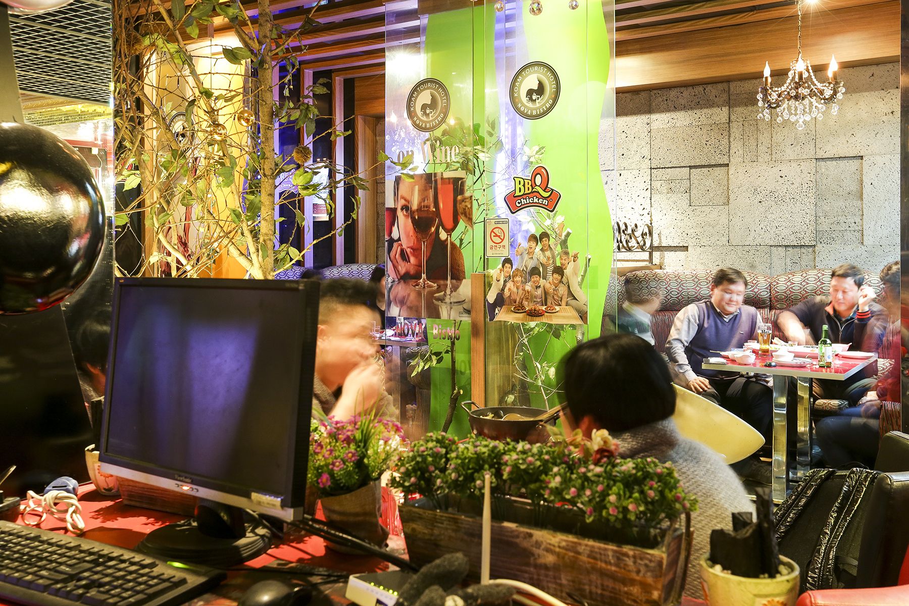 Un restaurant avec un pilier vert, une enseigne indiquant « poulet grillé », et un groupe de personnes qui déjeunent ou dînent.