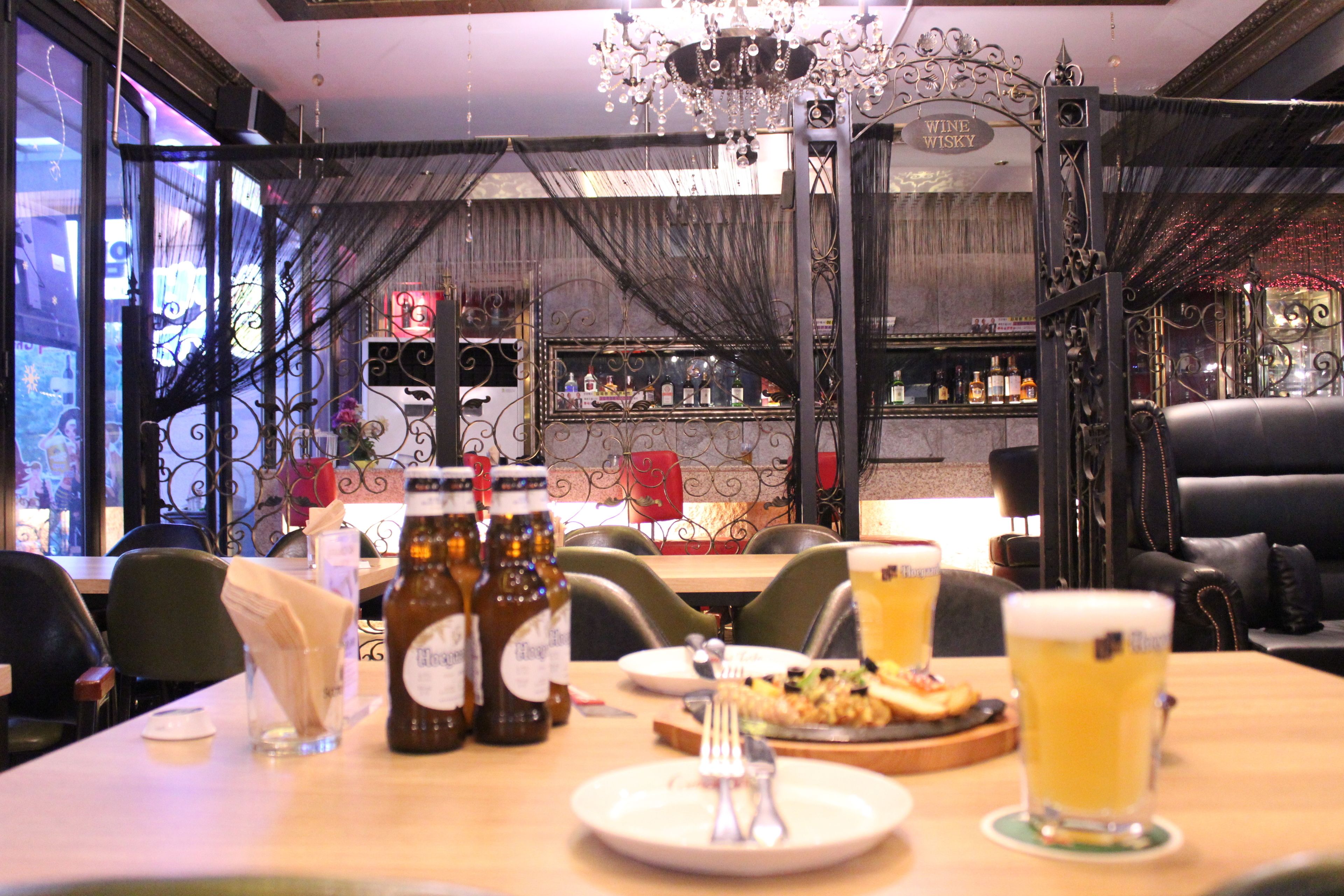 A restaurant interior with a bar area, dining tables, chairs, and a chandelier.
