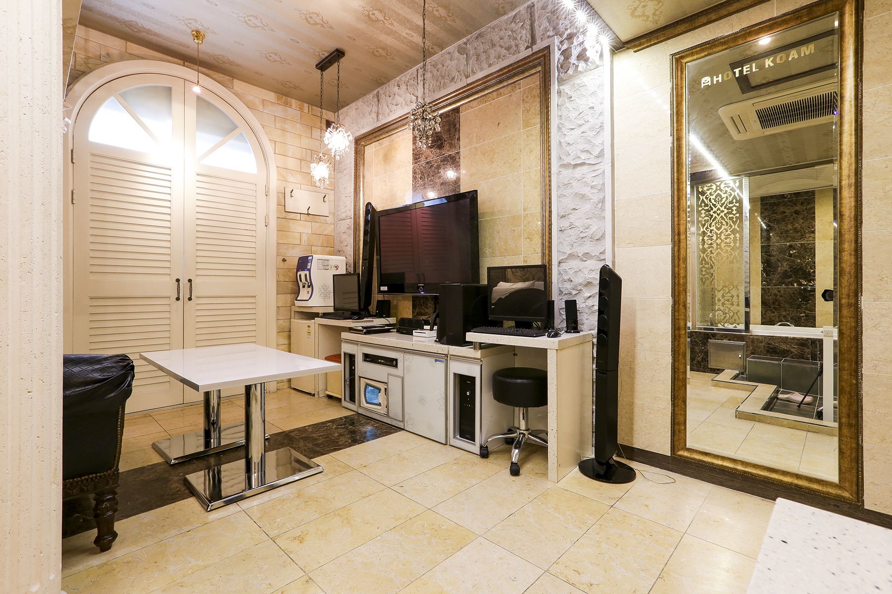 A compact hotel room with a kitchenette, a flat-screen TV, a desk with a chair, and a large mirror.
