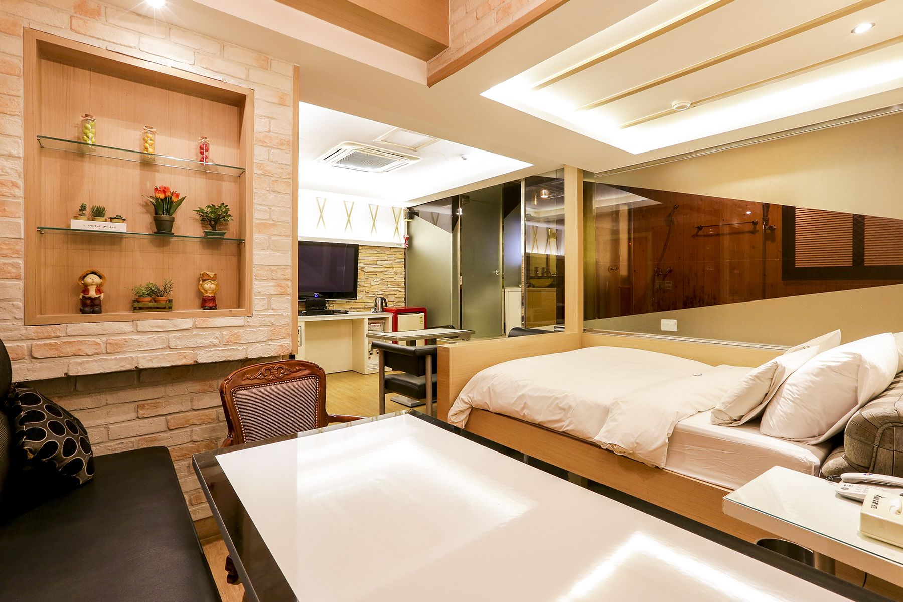 A hotel room with a bed, a desk, a chair, a TV, a mirror, and a shelf with decorative items.