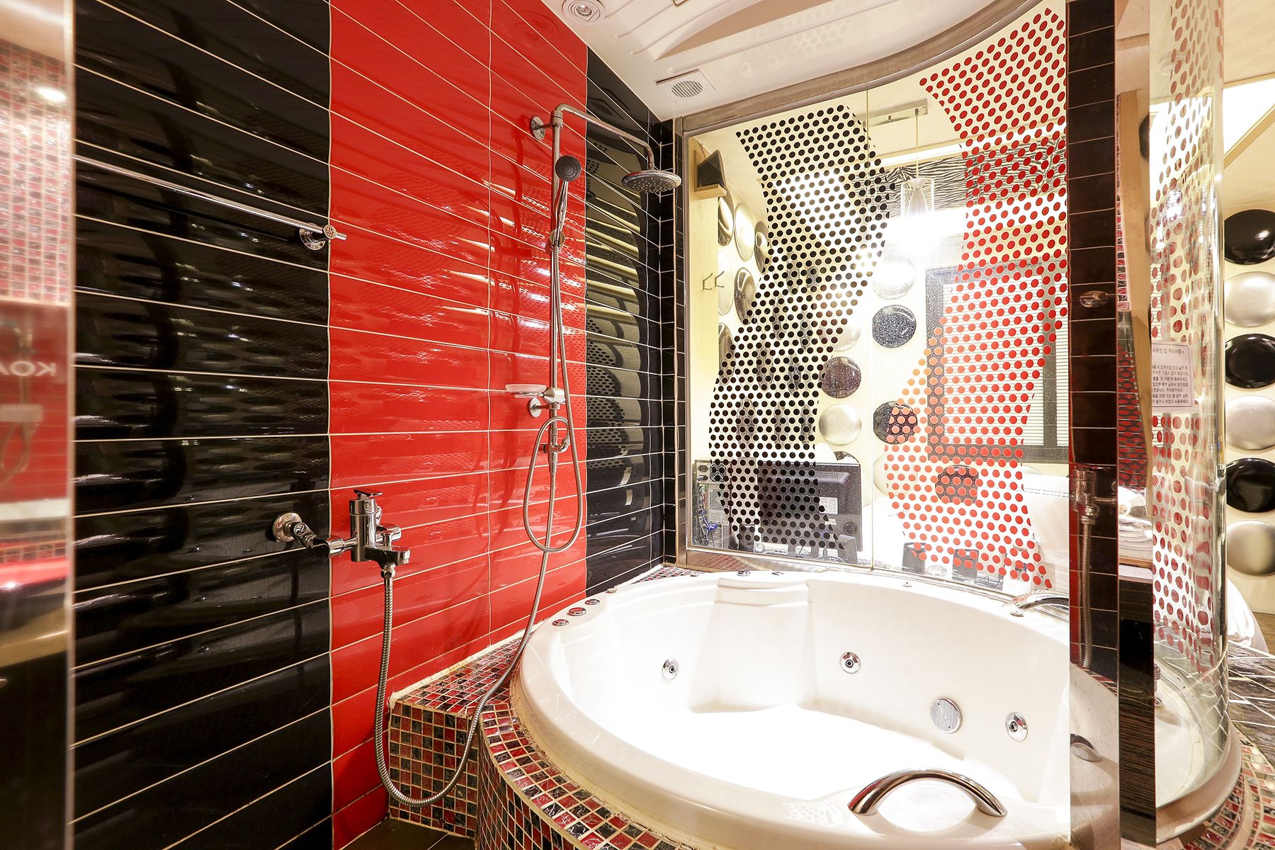 A modern bathroom with a large bathtub, red and black tiled walls, and a shower area with a glass partition.