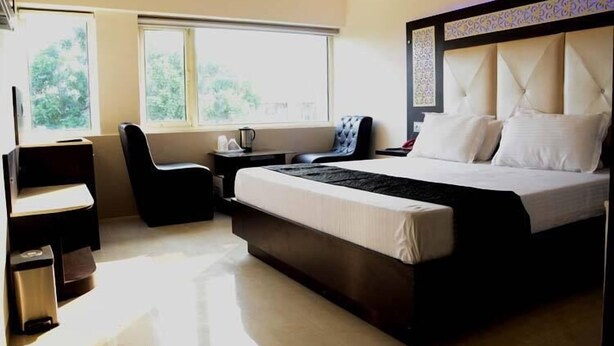 Quarto de hotel moderno com uma cama grande, uma escrivaninha, uma cadeira e duas janelas.