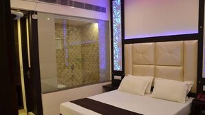Quarto de hotel moderno com uma cama grande, chuveiro em cabine de vidro e um painel decorativo na parede.