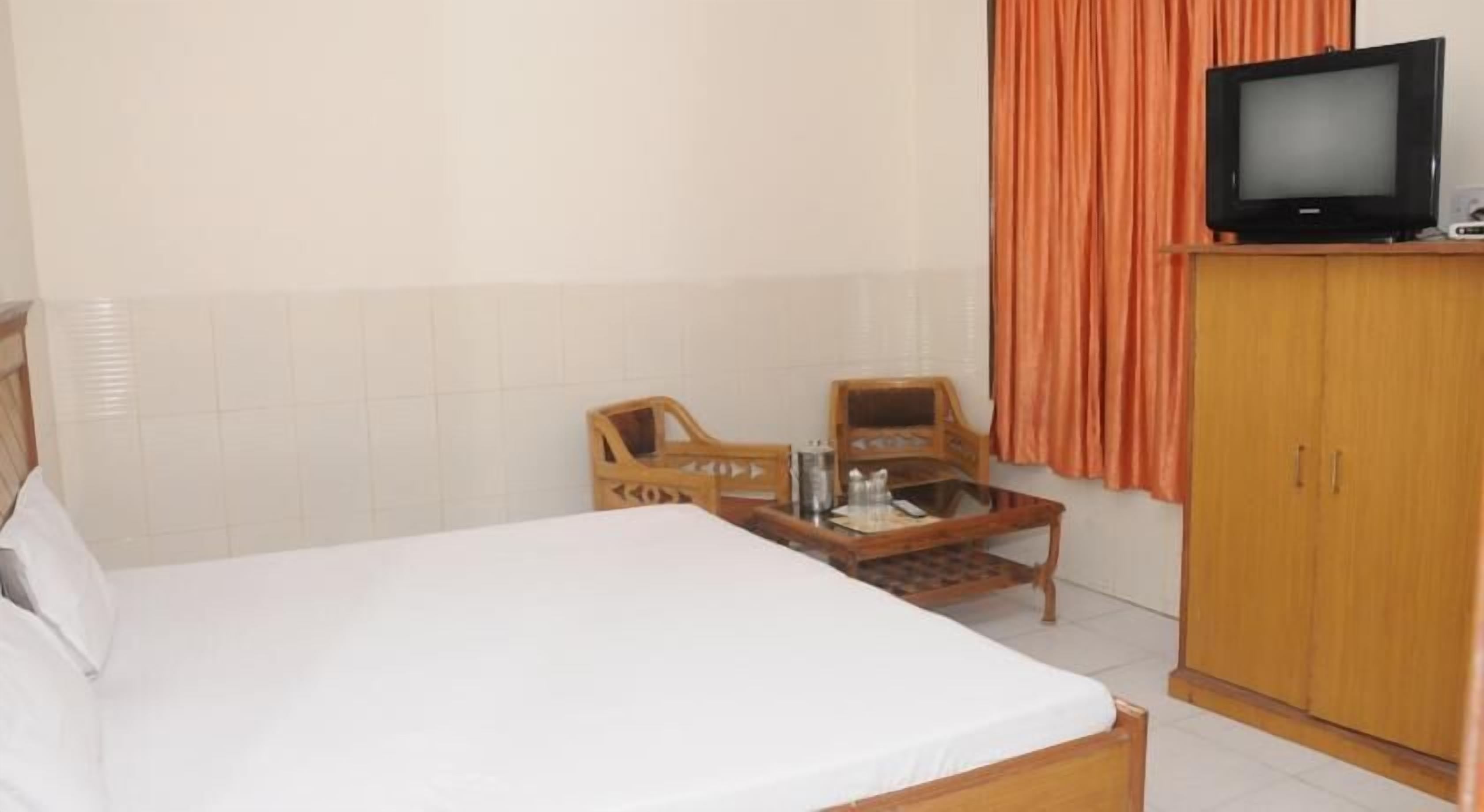A hotel room with a bed, a wooden wardrobe, a television, and two wooden chairs.