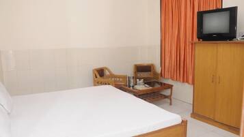 A hotel room with a bed, a wooden wardrobe, a television, and two wooden chairs.