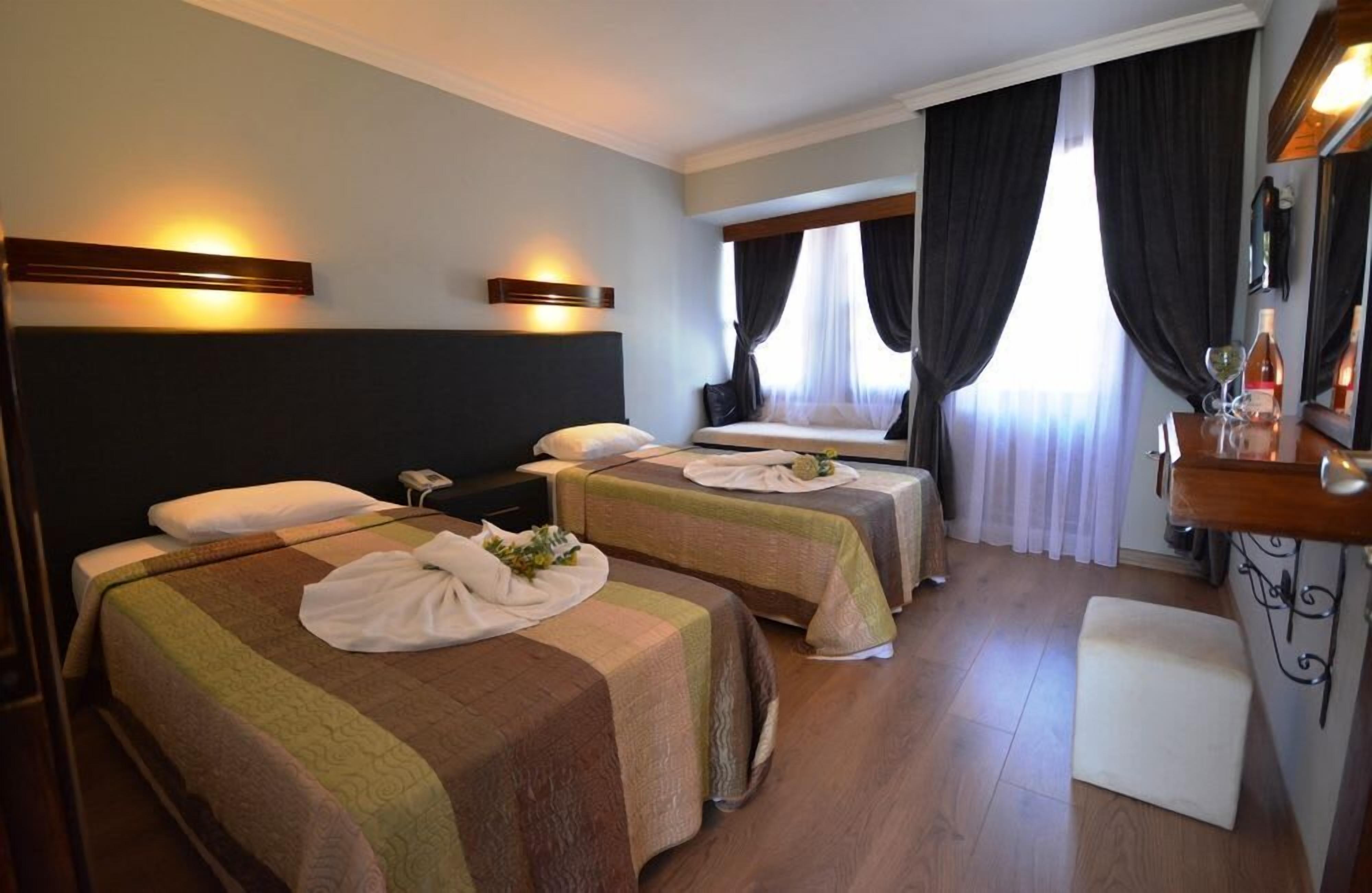 A hotel room with two beds, a desk, a chair, and a window with curtains.