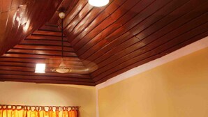A room with two wooden beds, a wooden ceiling, and a window with curtains. - Chandragiri Bungalow (Vythiri)