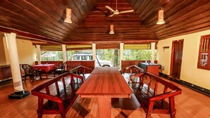 A long wooden dining table with benches, a ceiling fan, and a view of the outdoors. - Chandragiri Bungalow (Vythiri)