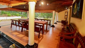 An indoor patio area with wooden flooring, a central table with chairs, and a fireplace. - Chandragiri Bungalow (Vythiri)