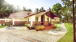 A house with a tiled roof, a porch with potted plants, and a paved driveway. - Chandragiri Bungalow (Vythiri)