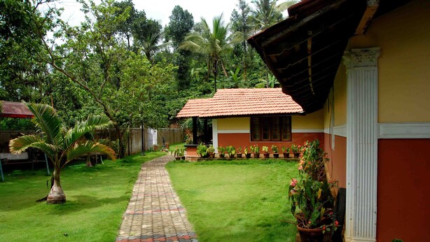 A house with a tiled roof, a paved pathway, and a well-maintained lawn. - Chandragiri Bungalow (Vythiri)