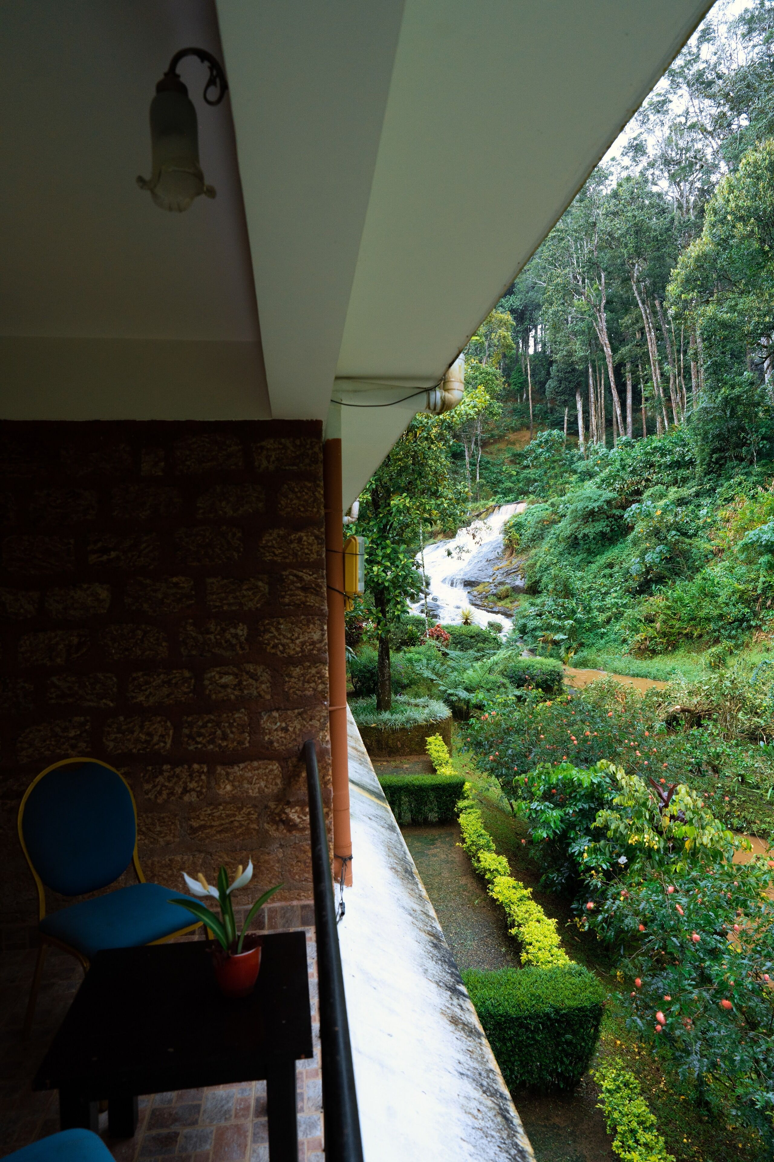 A balcony with a view of a lush garden and a waterfall.