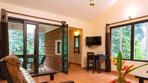 Una habitación con un gran ventanal corredera que da a un balcón, un área de comedor con mesa y sillas, un televisor montado en la pared y una planta en maceta sobre una mesa.
