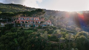 A multi-story building with a red facade, surrounded by dense greenery and hills. - Intur Residence (Marciana Marina)