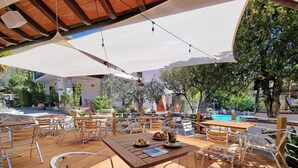 Ein Außenbereich mit Holztischen und -stühlen, im Hintergrund ein Pool und eine überdachte Terrasse.