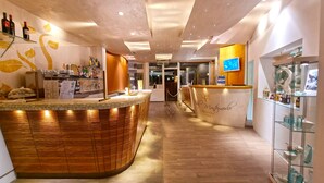 Ein Hotel-Rezeptionsbereich mit einer gebogenen Holztresen, einer Glastheke mit Flaschen und einem Empfangsbereich mit einem Computermonitor.
