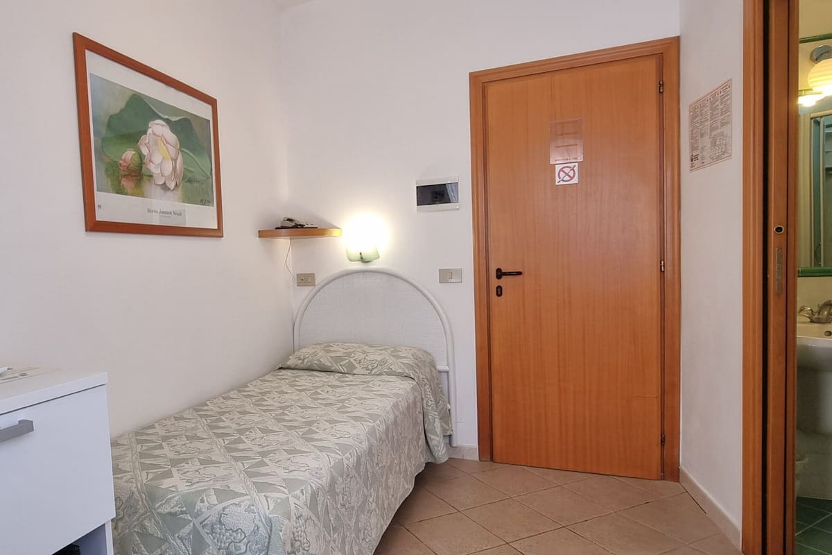 Ein Schlafzimmer mit Bett, Nachttisch, Spiegel, Wandleuchte und einer Tür zu einem Badezimmer.