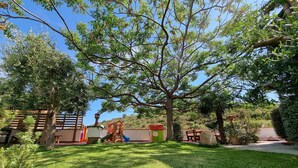 Ein gepflegter Garten mit verschiedenen Bäumen und Sträuchern, einer Holzterrasse und einer kleinen Spielbereiches für Kinder.
