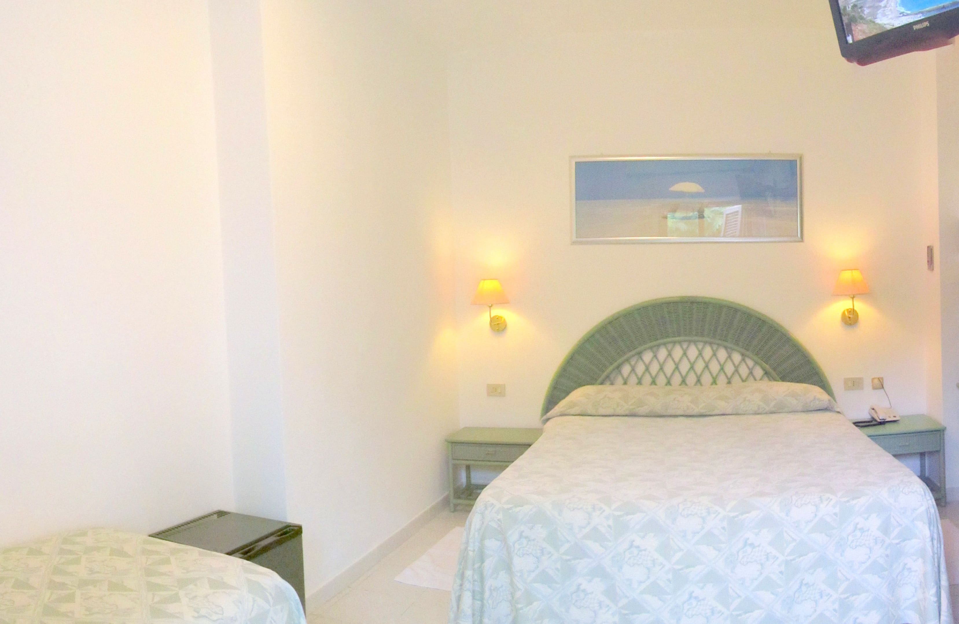A bedroom with a bed, two bedside tables, a nightstand, a lamp, and a painting on the wall.