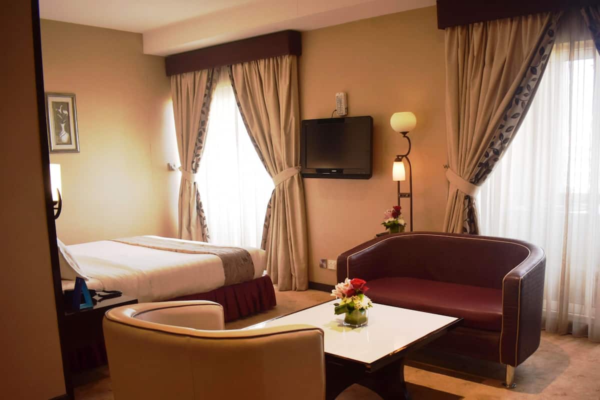 A hotel room with a bed, a sofa, a desk, a TV, and a lamp.