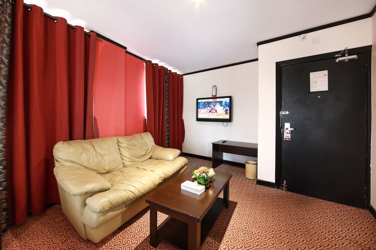 A room with a beige sofa, a wooden coffee table, a TV on the wall, and a black door.
