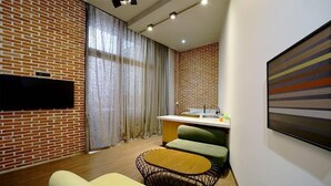 Una sala moderna con pared de ladrillo, un televisor de pantalla plana, un comedor con mostrador de cocina y un sofá verde.