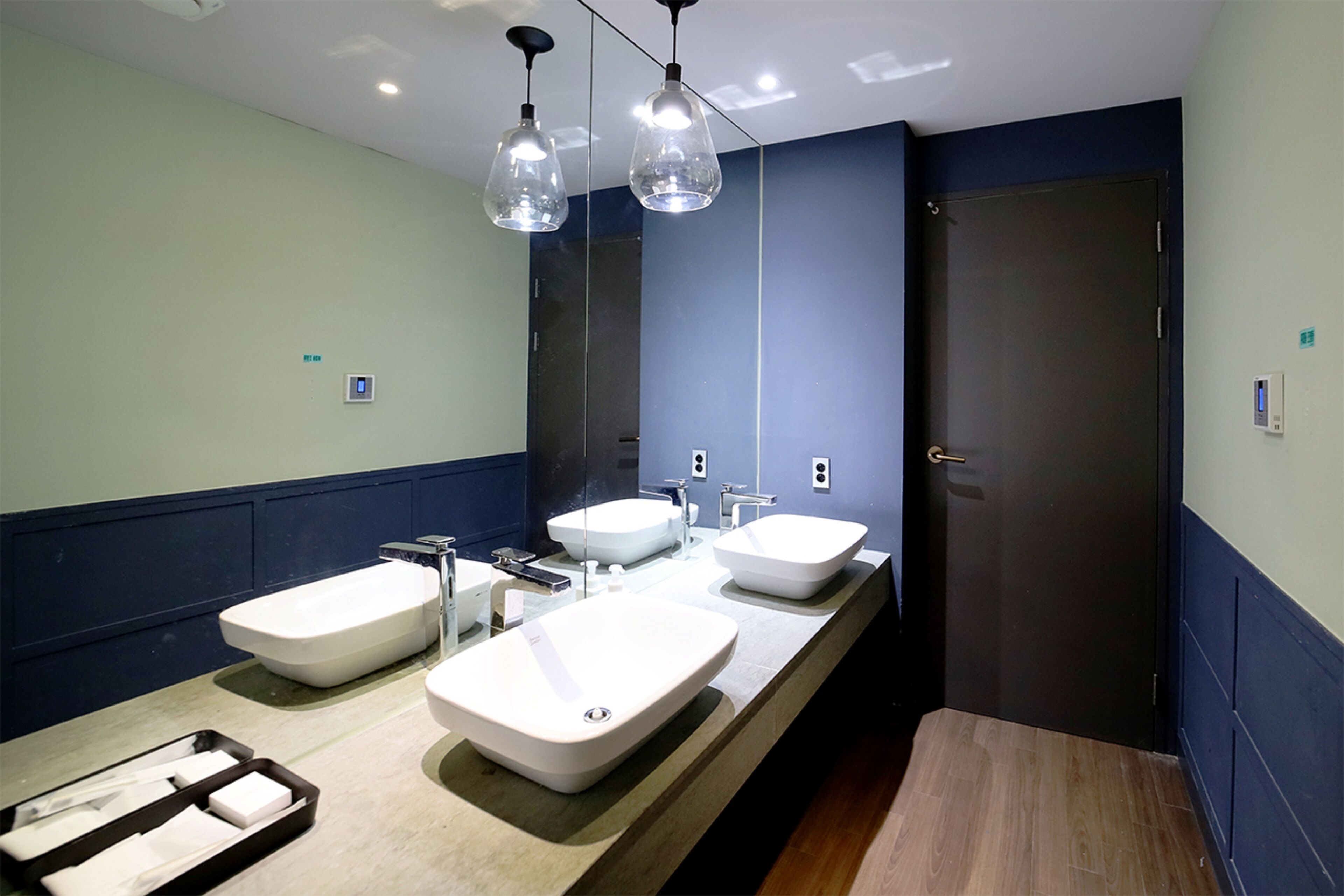 A modern bathroom with three sinks, a mirror, and pendant lights.