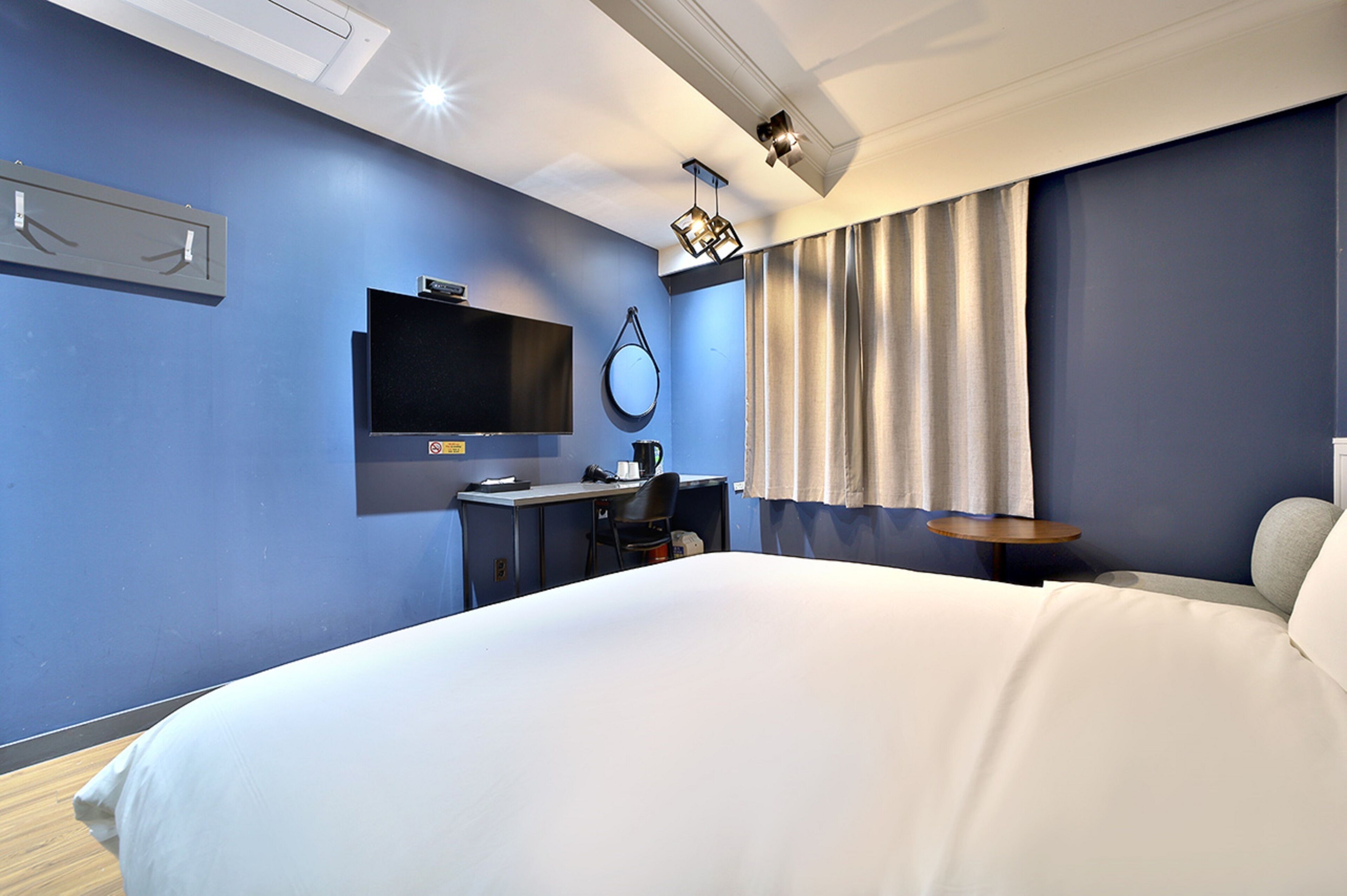 A modern hotel room with a large bed, a desk, a flat-screen TV, and a ceiling-mounted light fixture.