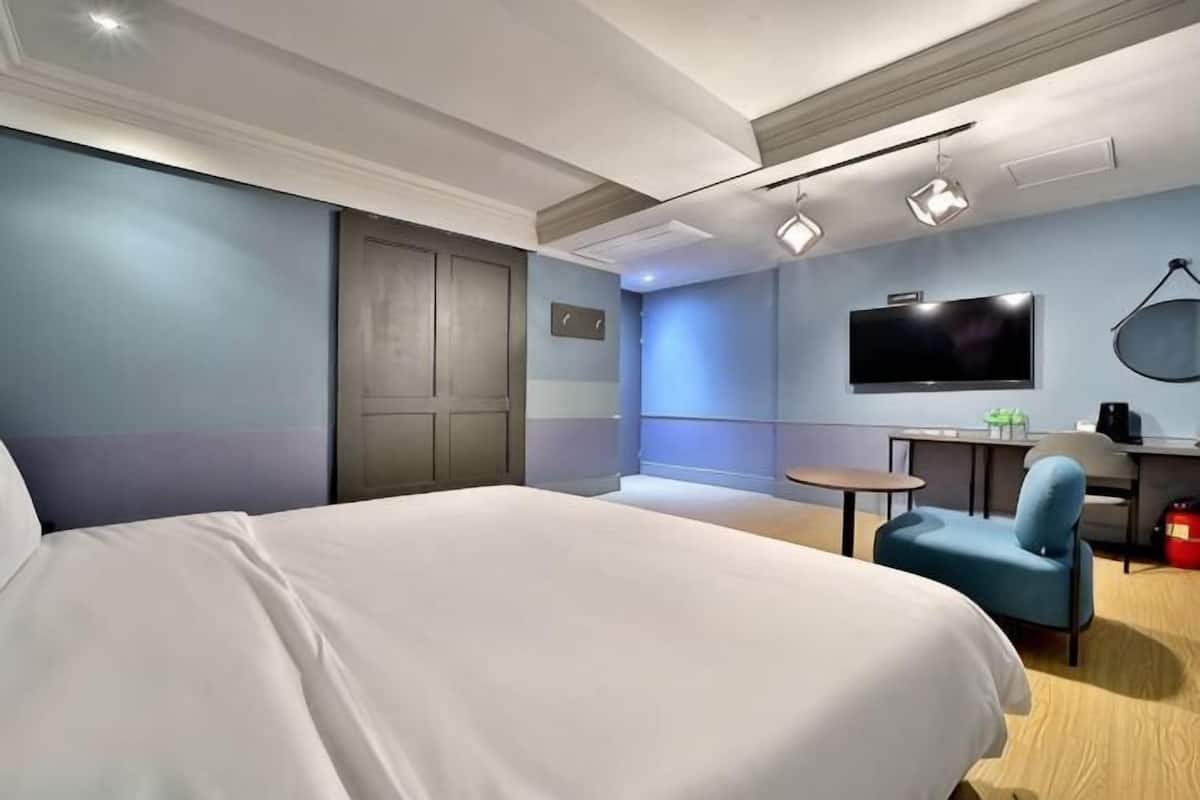 Una habitación de hotel con una cama, un escritorio, una silla, un televisor y una puerta.