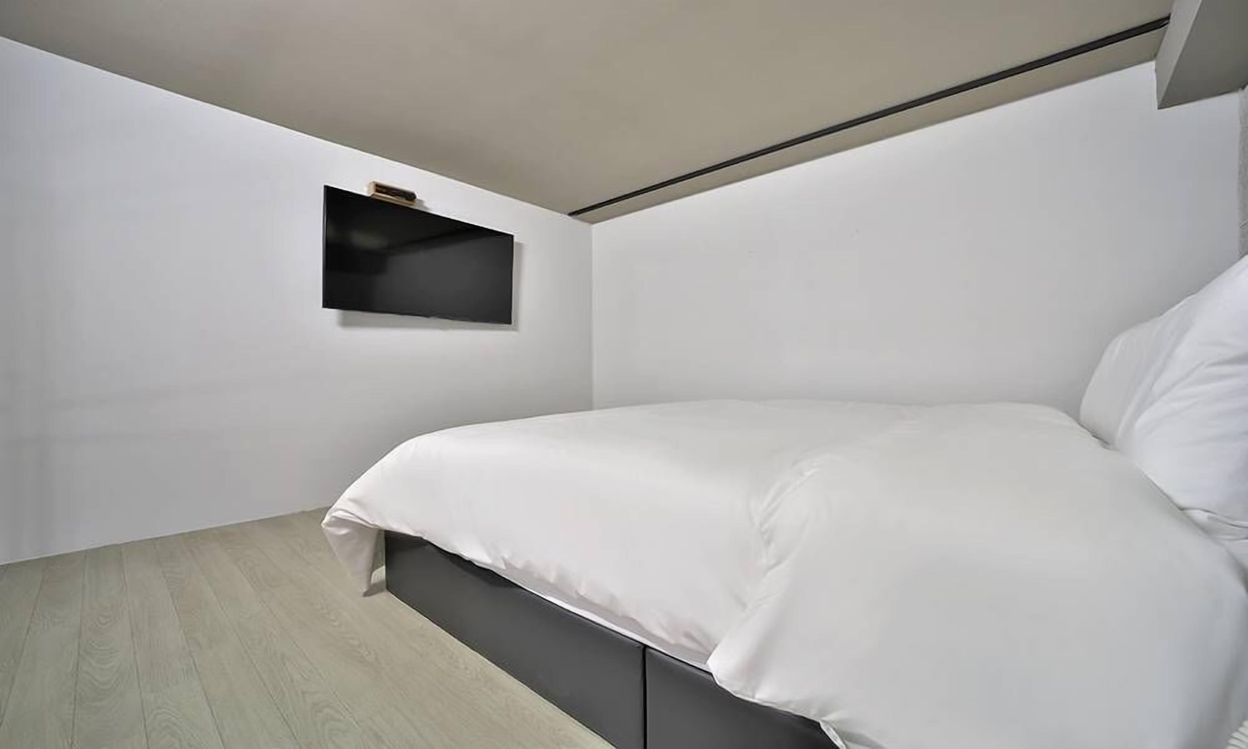 Een moderne slaapkamer met een bed, een klein schapje en een licht houten vloer.