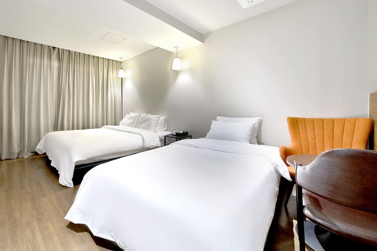 Una habitación de hotel con dos camas, piso de madera, una silla y una mesita de noche.