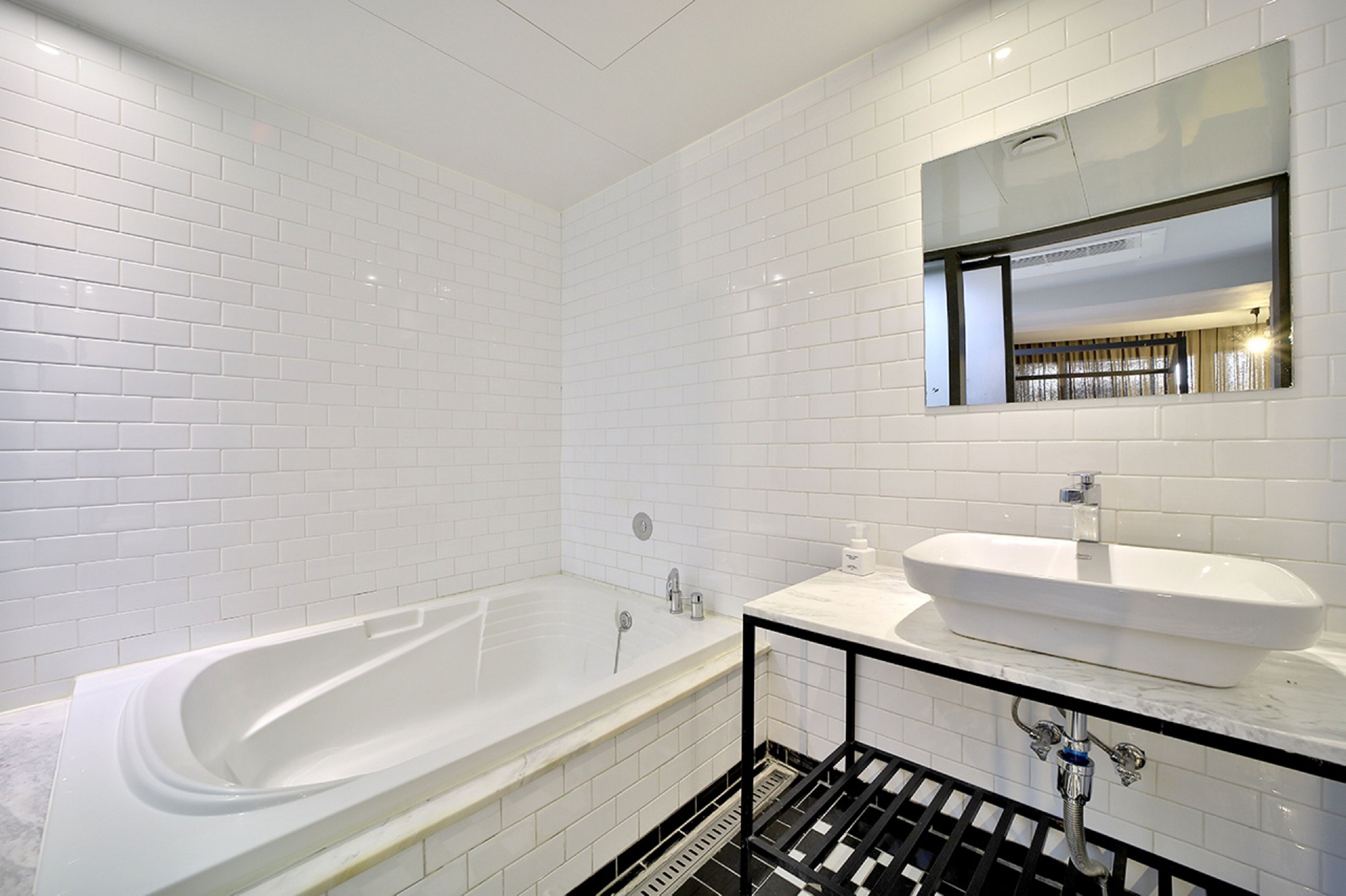 A modern bathroom with white subway tiles, a freestanding bathtub, a white sink, and a black metal rack.