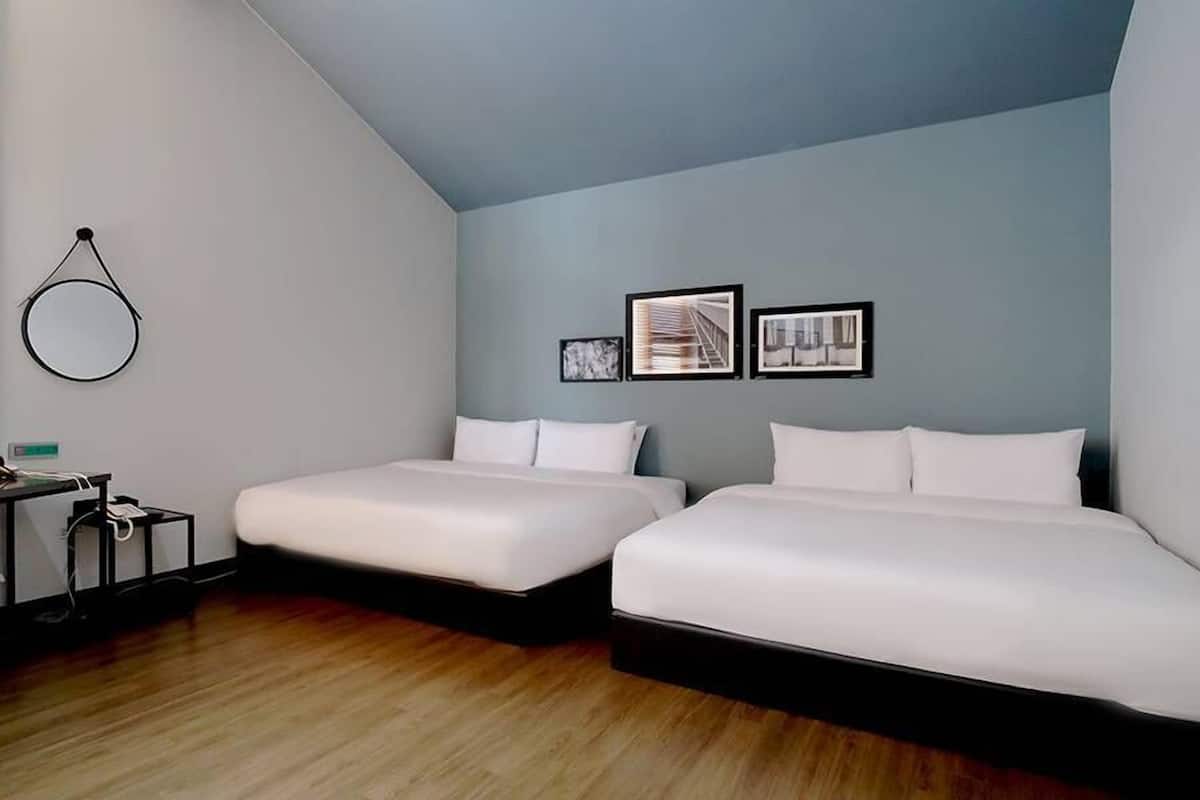 Una habitación de hotel moderna con dos camas individuales, un escritorio con silla y un espejo redondo en la pared.