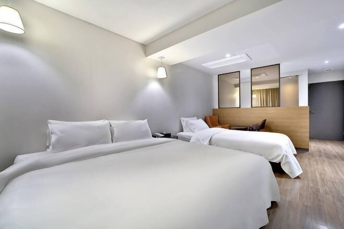 Una habitación de hotel moderna con una cama grande, una cama más pequeña, un cabecero de madera y un espejo amplio.