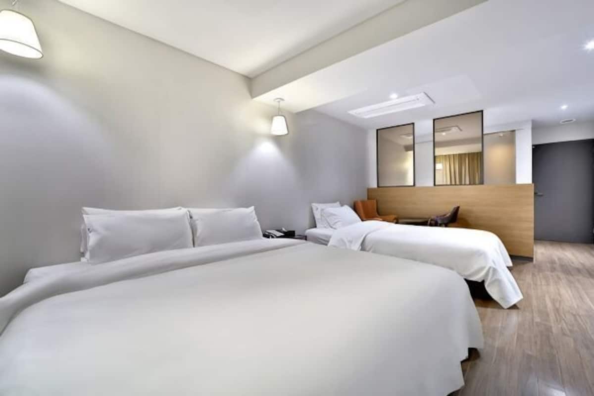 Una habitación de hotel moderna con una cama grande, una cama mÔs pequeña, un cabecero de madera y un espejo amplio.