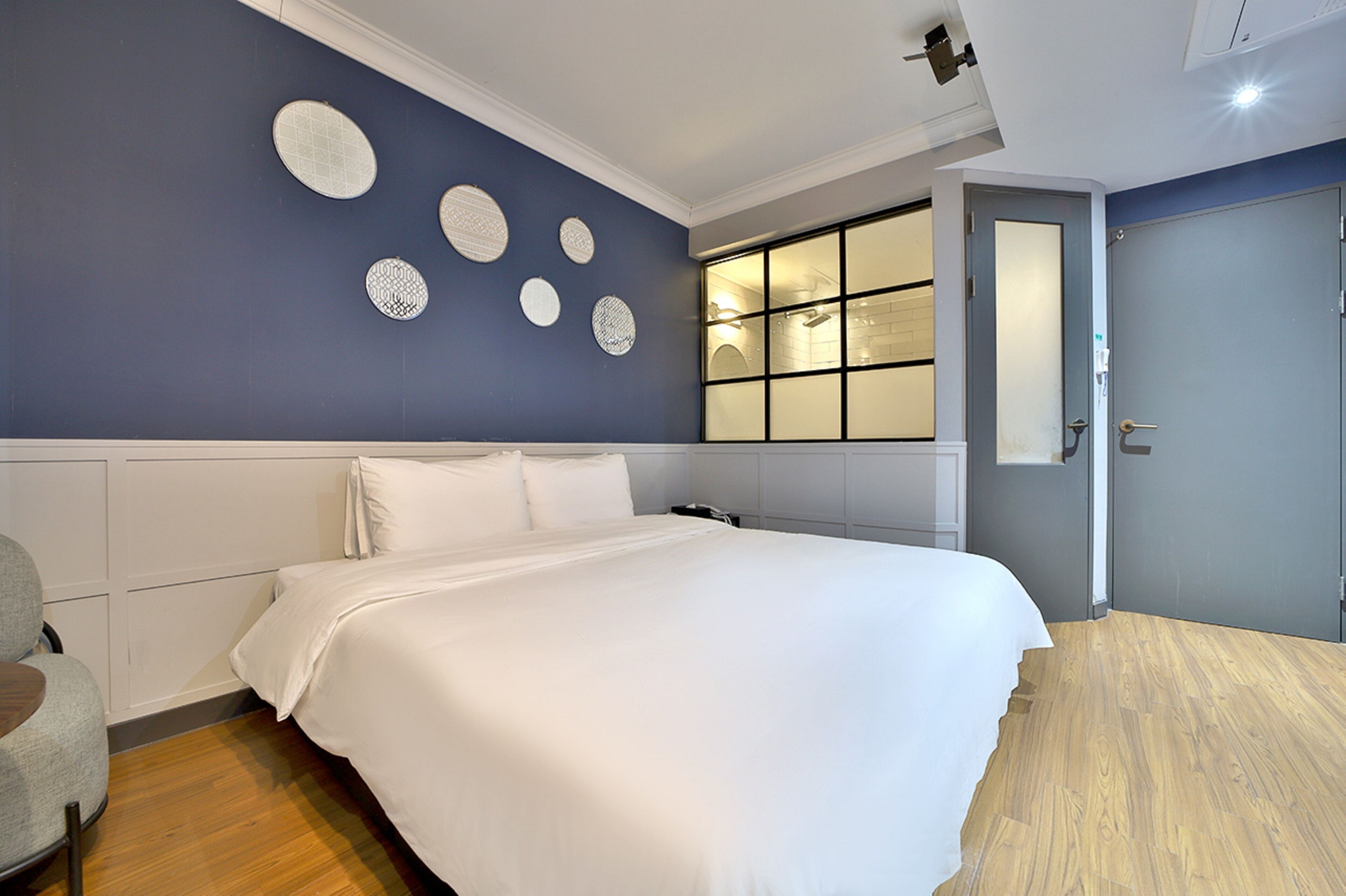 Une chambre à coucher avec un grand lit, une table de chevet, une chaise et une fenêtre avec des stores.