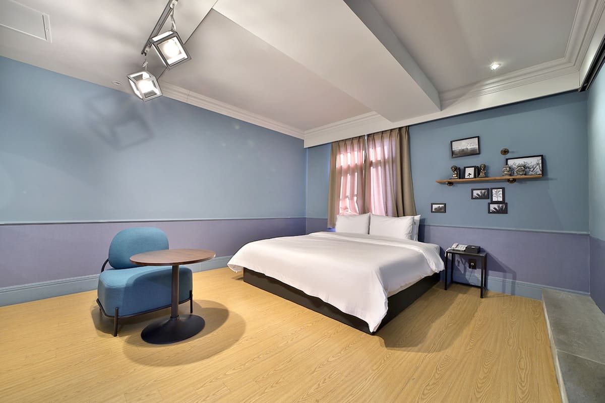 Habitación de hotel con cama, un sillón azul, una mesa redonda y una mesita de noche con teléfono.