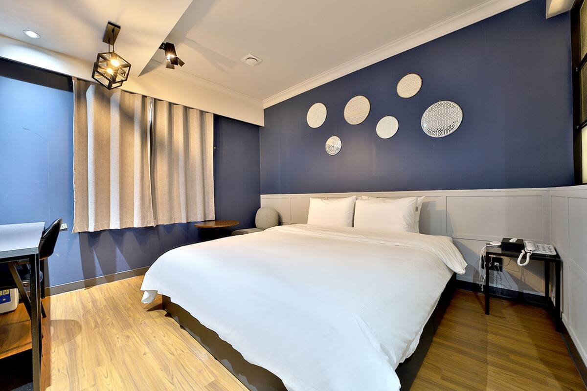 Una habitación de hotel moderna con una cama grande, un escritorio y una silla. Hay decoraciones en la pared y un teléfono en la mesita de noche.