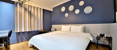 A modern hotel room with a large bed, a desk, and a chair. There are wall decorations and a telephone on the nightstand.