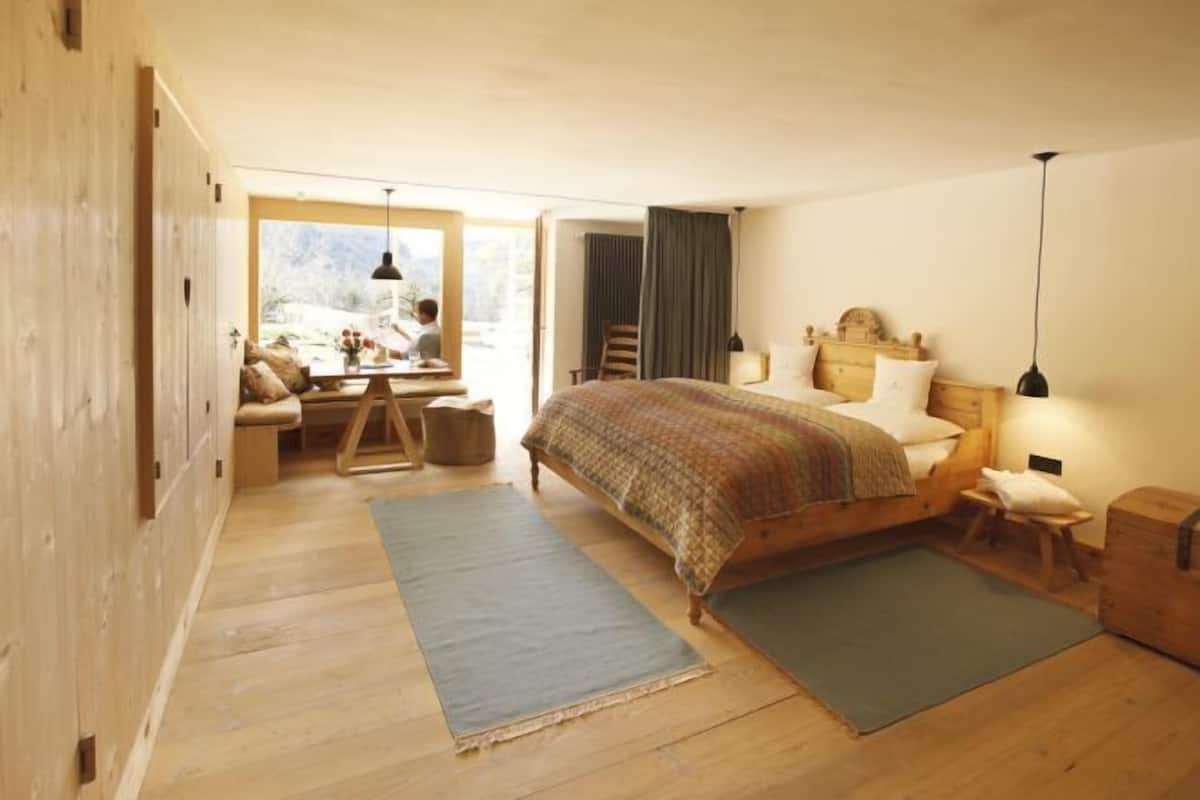 A cozy bedroom with a wooden bed, a desk, and a view of the outdoors.