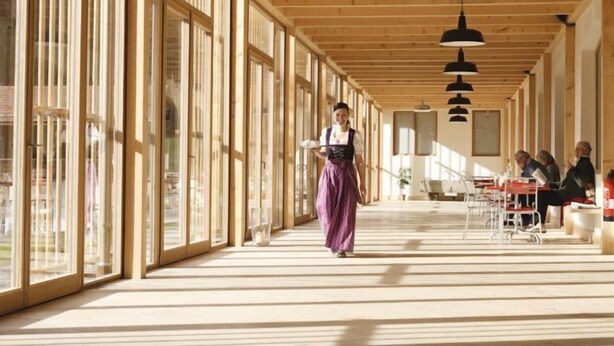 A spacious indoor area with large windows, wooden beams, and hanging pendant lights.