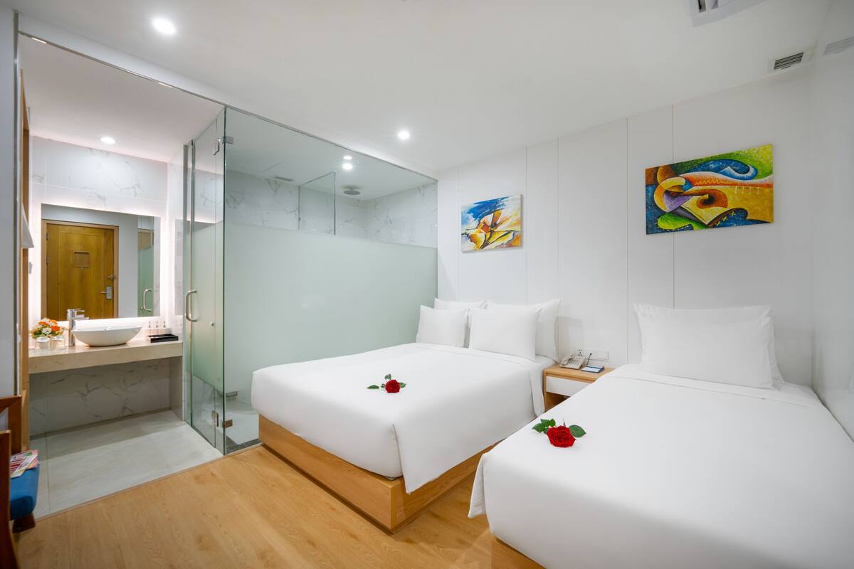 A hotel room with two beds, a bathroom with a glass shower enclosure, and artwork on the walls.
