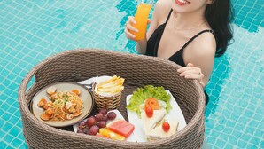 Una persona en una piscina sosteniendo una cesta con comida y una bebida.