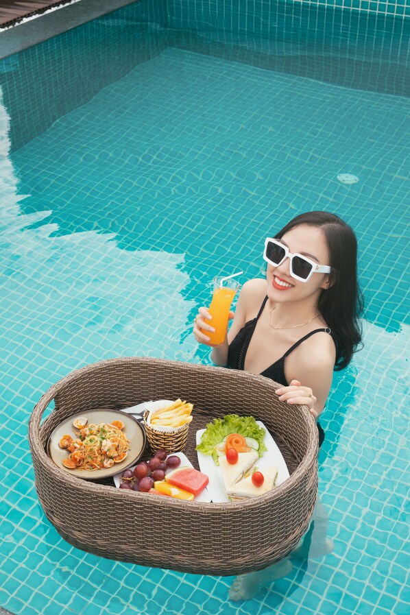 A person in a swimming pool holding a basket with food and a drink. - Solara Diamond Hotel (Da Nang)