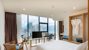 Habitación de hotel con una cama grande, un escritorio con ordenador, una silla, televisión y vistas a la ciudad.