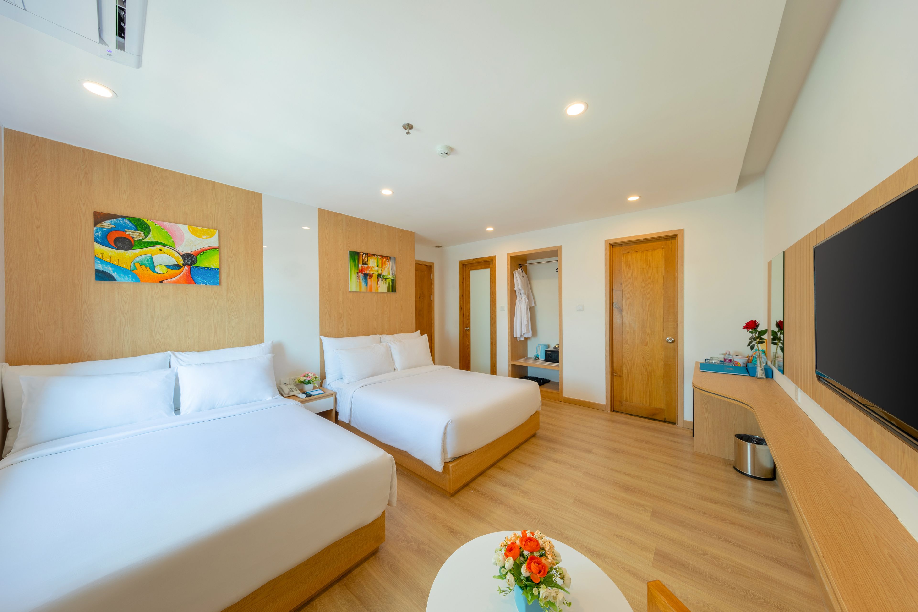 A hotel room with two beds, a small table with flowers, a TV, and artwork on the walls.