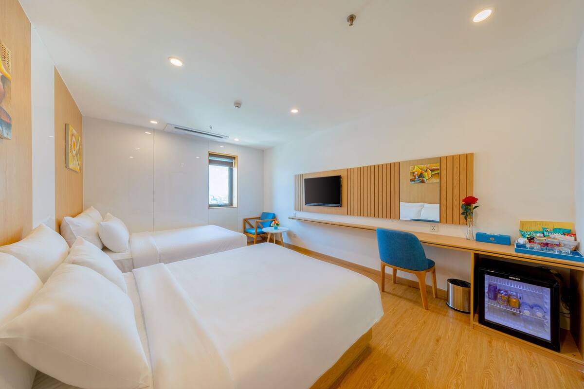 A hotel room with two beds, a desk, a chair, a television, and a minibar.