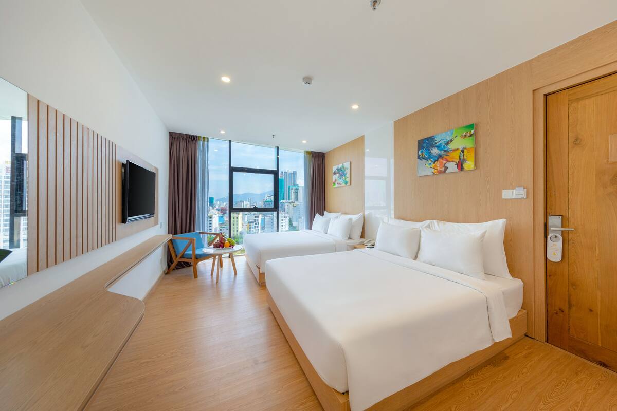 A hotel room with two beds, a TV, a city view, and a wooden door.