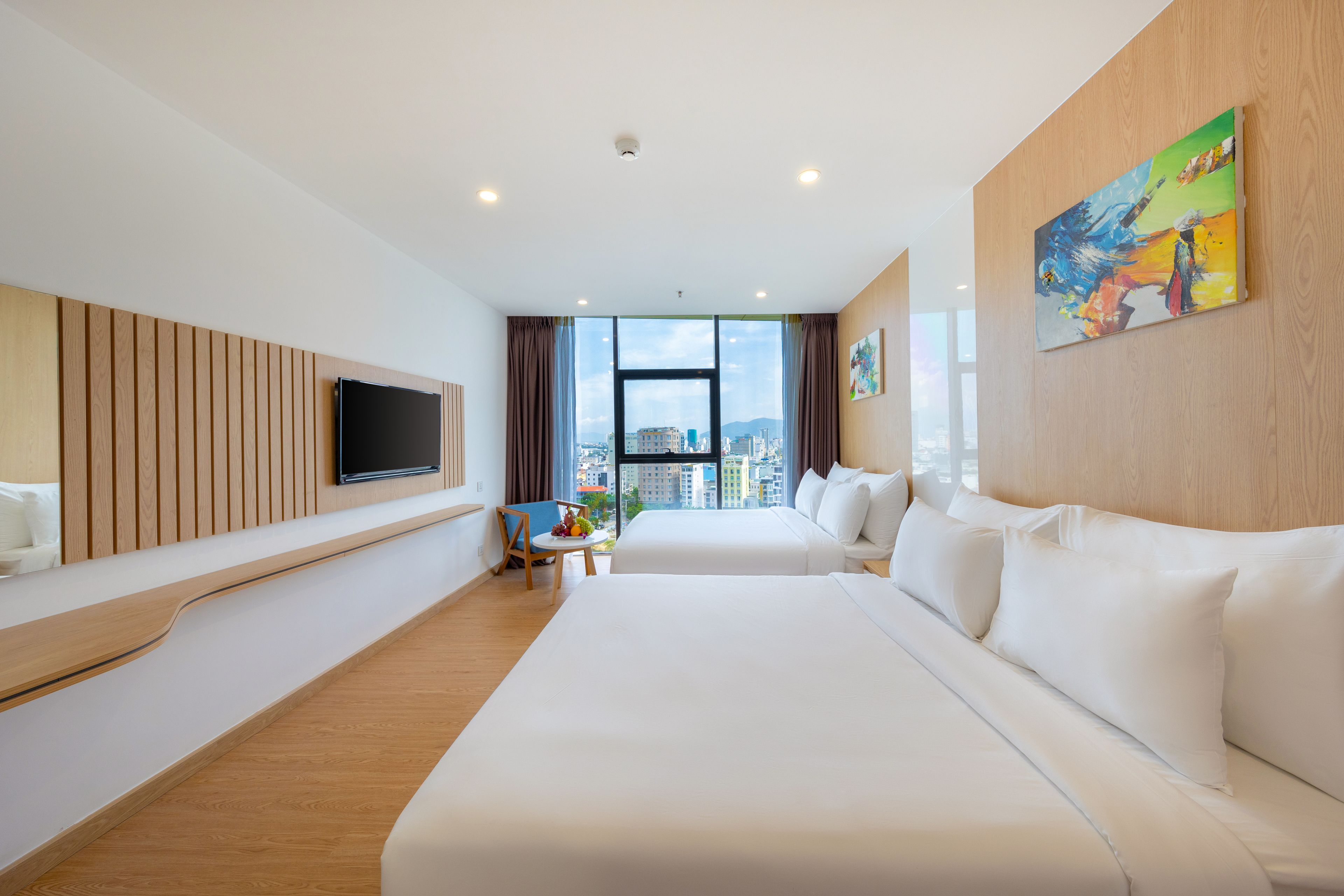 Ein modernes Hotelzimmer mit zwei Betten, einem wandmontierten Flachbildfernseher, einer Essecke und einem großen Fenster mit Blick auf die Stadt.